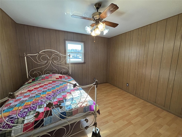 bedroom with light hardwood / wood-style floors, wooden walls, and ceiling fan