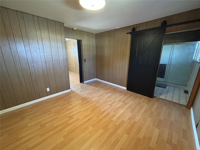 unfurnished bedroom featuring wooden walls, a barn door, and light hardwood / wood-style flooring