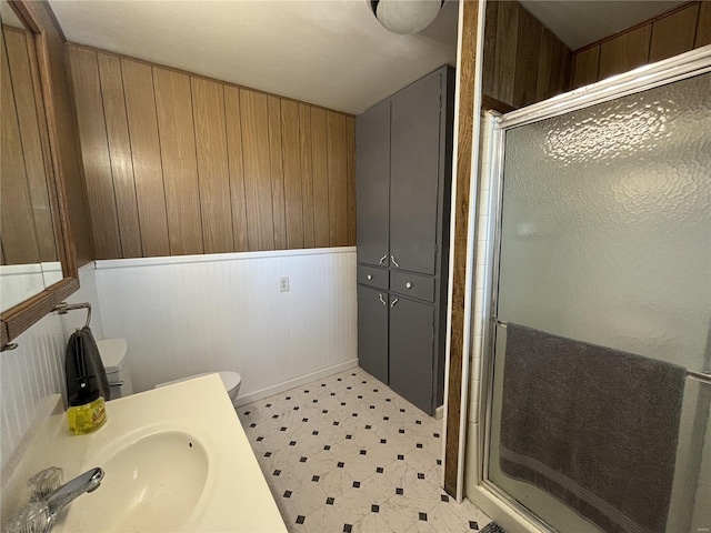 bathroom featuring sink, wooden walls, toilet, and an enclosed shower