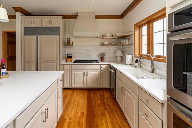 kitchen with light hardwood / wood-style flooring, custom range hood, sink, crown molding, and appliances with stainless steel finishes