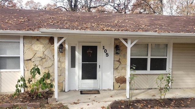 doorway to property featuring roof with shingles and stone siding