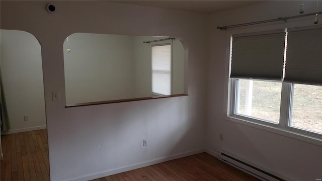 spare room featuring arched walkways, a baseboard radiator, baseboards, and hardwood / wood-style floors