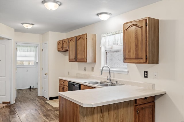 kitchen with light wood-type flooring, kitchen peninsula, sink, and black dishwasher