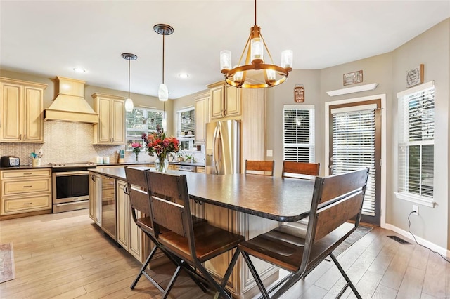 kitchen featuring appliances with stainless steel finishes, premium range hood, light wood-type flooring, and pendant lighting