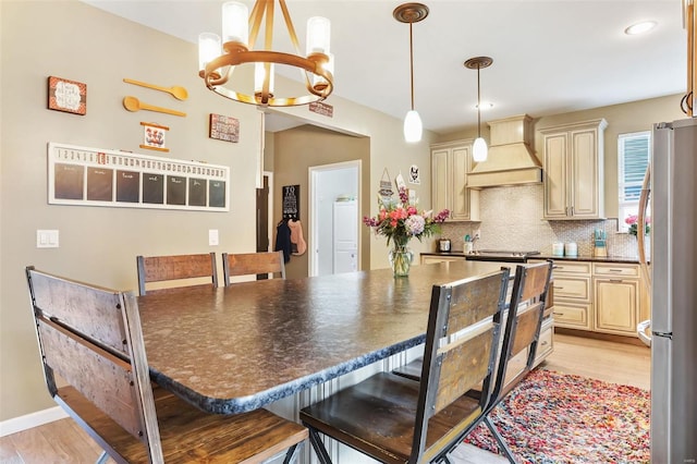 kitchen featuring light hardwood / wood-style flooring, custom range hood, a breakfast bar, stainless steel refrigerator, and tasteful backsplash