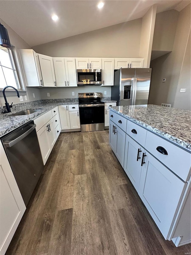 kitchen with light stone counters, stainless steel appliances, white cabinetry, vaulted ceiling, and a sink