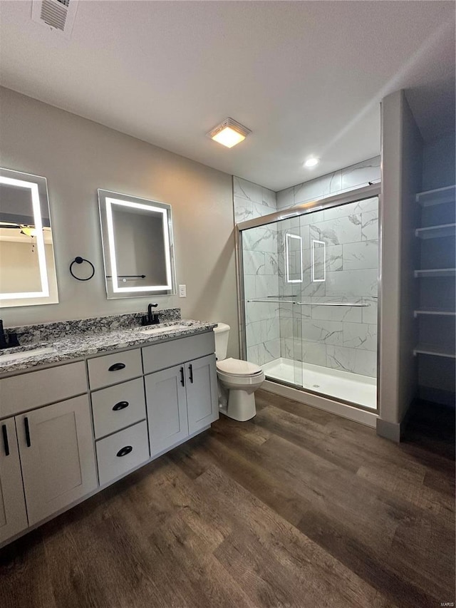 full bath with a marble finish shower, double vanity, visible vents, a sink, and wood finished floors