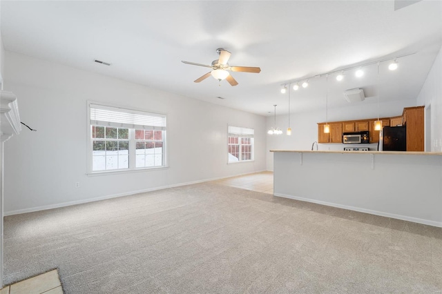 unfurnished living room featuring rail lighting, light colored carpet, and ceiling fan with notable chandelier