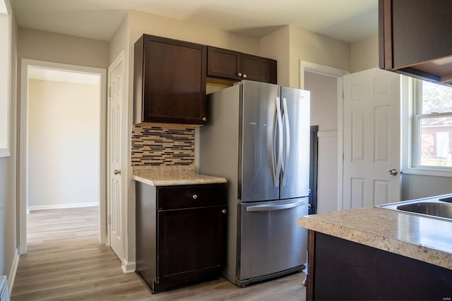 kitchen with light hardwood / wood-style flooring, dark brown cabinetry, backsplash, and stainless steel refrigerator