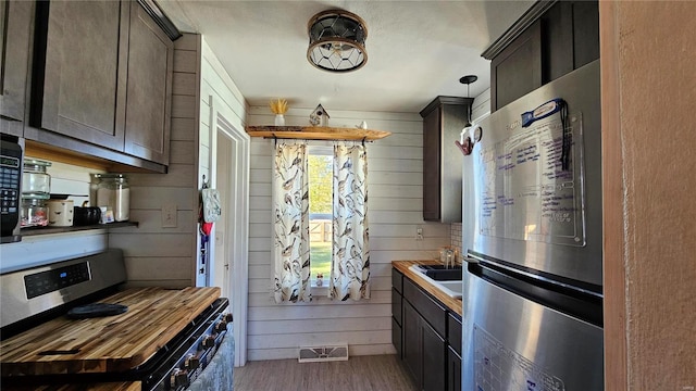 kitchen with stove, wood-type flooring, stainless steel refrigerator, wood walls, and butcher block counters