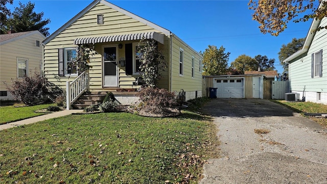 bungalow-style home with central air condition unit, a front yard, an outbuilding, and a garage