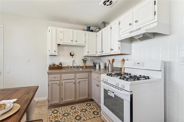 kitchen featuring light tile patterned floors, gas range gas stove, a sink, decorative backsplash, and under cabinet range hood