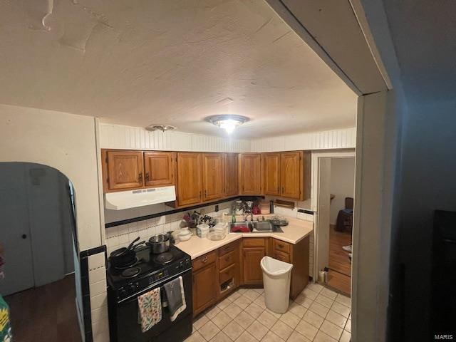 kitchen featuring sink, black electric range oven, decorative backsplash, and light wood-type flooring