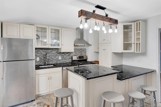 kitchen featuring wall chimney exhaust hood, sink, a breakfast bar, appliances with stainless steel finishes, and decorative light fixtures