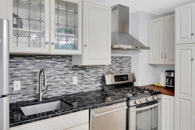 kitchen featuring stainless steel appliances, dark stone counters, white cabinets, wall chimney exhaust hood, and sink