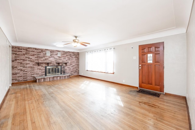 unfurnished living room featuring a brick fireplace, brick wall, light wood-type flooring, and ceiling fan