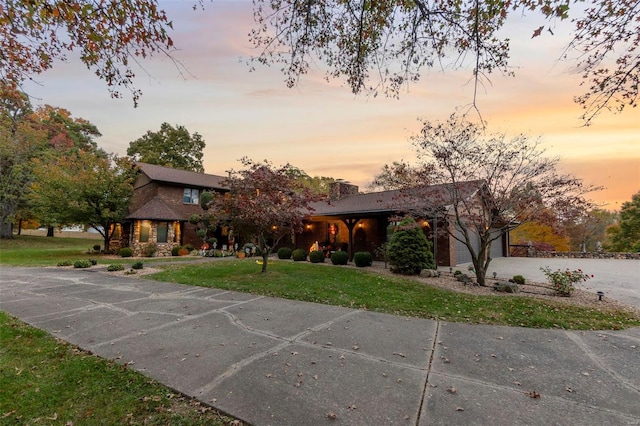 view of front of property featuring a garage, a chimney, driveway, and a lawn