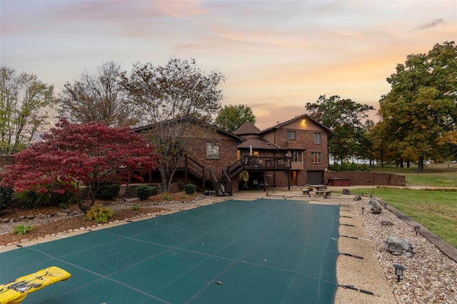 exterior space with a covered pool, a patio area, stairs, brick siding, and a deck