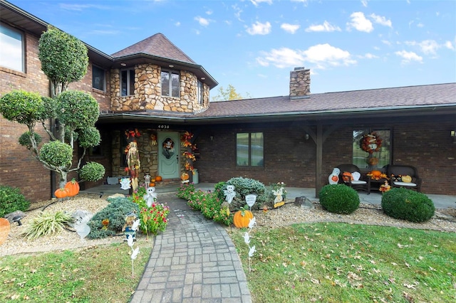 view of front facade featuring a porch, brick siding, stone siding, and a chimney