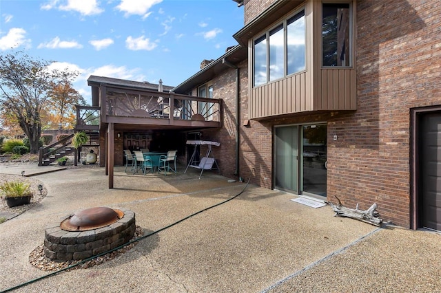 rear view of property featuring a fire pit, brick siding, a patio, a wooden deck, and outdoor dining area