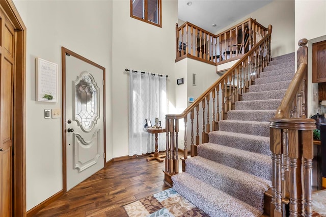 foyer entrance with a high ceiling, dark wood-style flooring, stairway, and baseboards