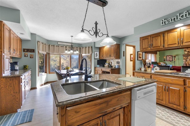 kitchen featuring a textured ceiling, a kitchen island with sink, a chandelier, white dishwasher, and sink