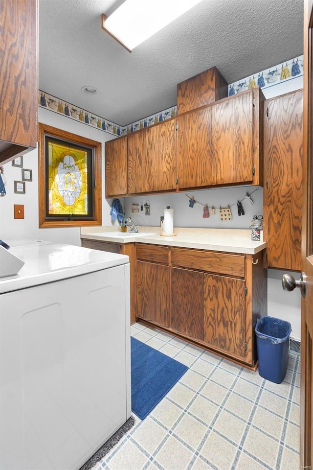 clothes washing area featuring a textured ceiling, washer / dryer, cabinet space, and a sink