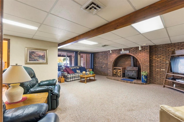 carpeted living room with a wood stove, a paneled ceiling, and brick wall