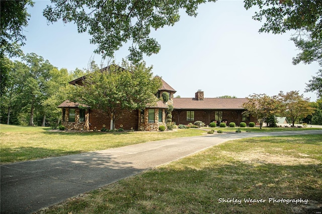 view of front of home with a chimney, a front yard, and curved driveway