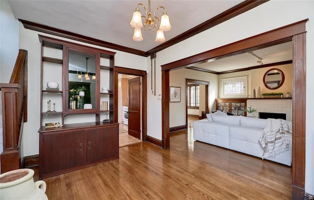 living room featuring crown molding, a notable chandelier, a tiled fireplace, and light wood-type flooring