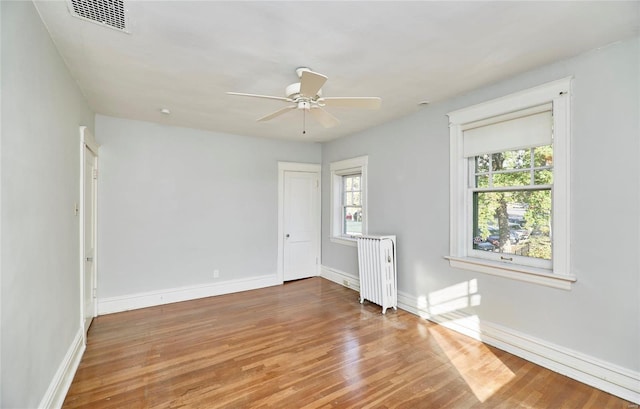 empty room featuring radiator, ceiling fan, wood-type flooring, and a wealth of natural light