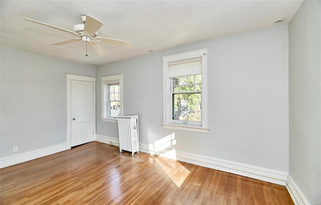 empty room featuring radiator, ceiling fan, wood-type flooring, and a wealth of natural light