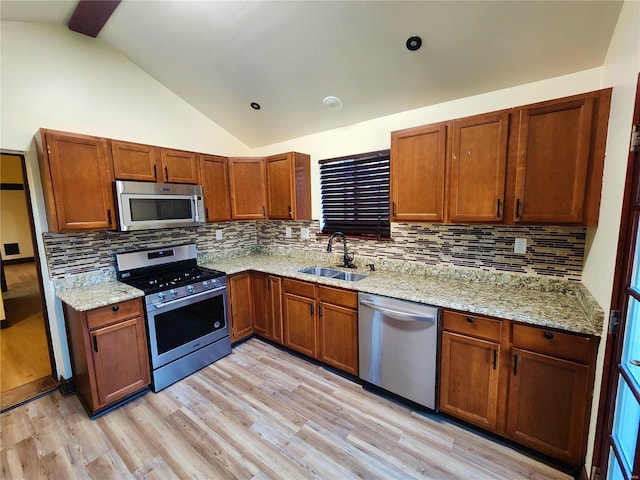 kitchen with light stone countertops, sink, backsplash, appliances with stainless steel finishes, and light wood-type flooring