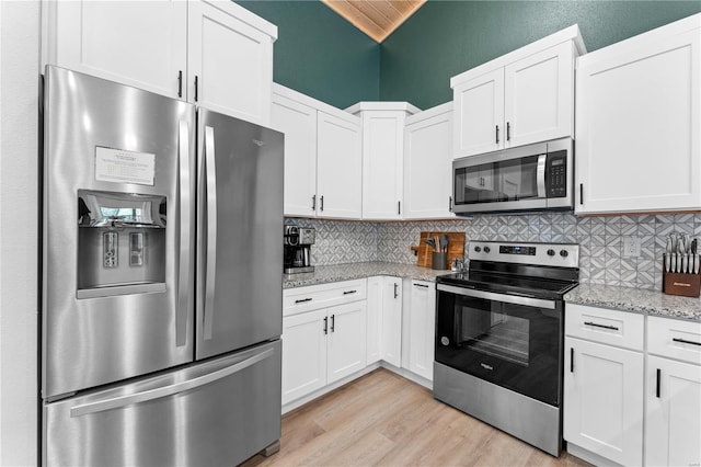 kitchen with light hardwood / wood-style flooring, light stone countertops, vaulted ceiling, white cabinets, and appliances with stainless steel finishes