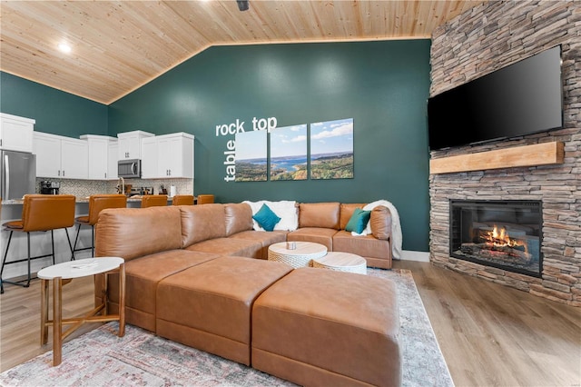 living room featuring wood ceiling, high vaulted ceiling, light hardwood / wood-style flooring, and a stone fireplace