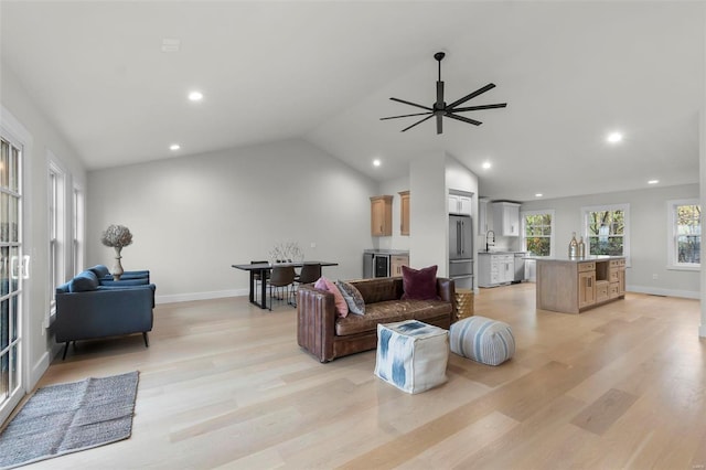 living room featuring sink, light hardwood / wood-style flooring, vaulted ceiling, and ceiling fan