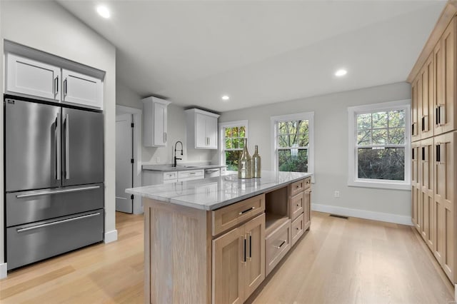 kitchen featuring light brown cabinetry, light wood-type flooring, a center island, white cabinetry, and stainless steel appliances