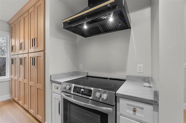 kitchen featuring wall chimney range hood, light hardwood / wood-style floors, stainless steel electric range, light stone counters, and light brown cabinets