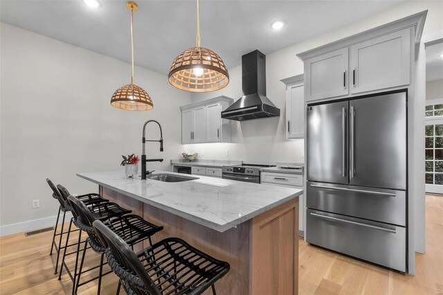 kitchen featuring light stone countertops, a kitchen breakfast bar, stainless steel appliances, wall chimney exhaust hood, and a kitchen island with sink