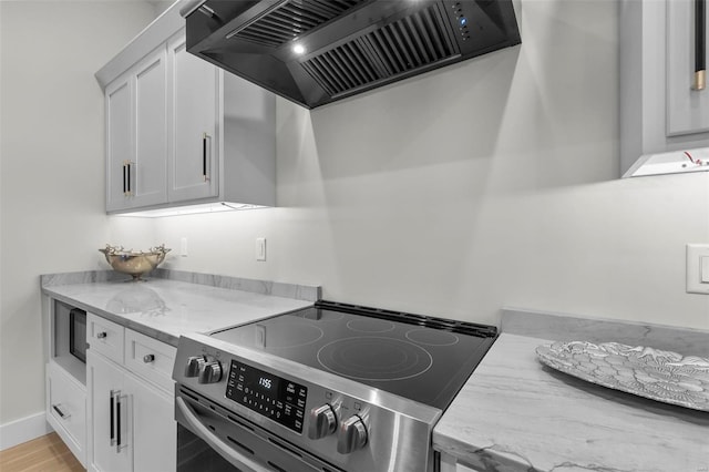 kitchen featuring light hardwood / wood-style flooring, light stone countertops, stainless steel range with electric cooktop, white cabinetry, and premium range hood