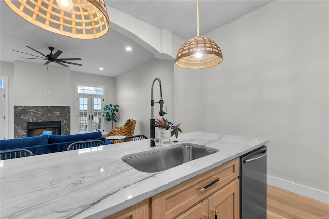 kitchen featuring light stone counters, a premium fireplace, light wood-type flooring, sink, and decorative light fixtures