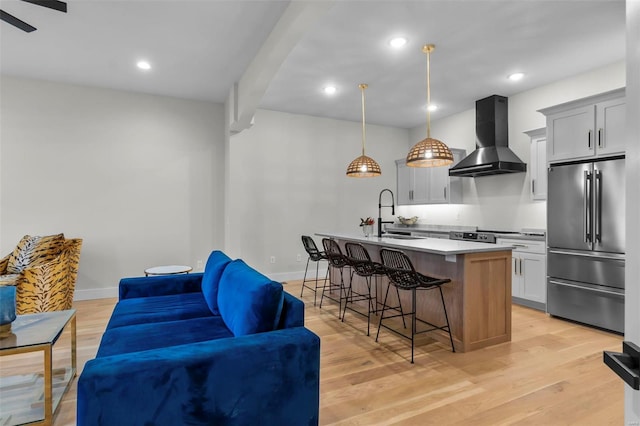 kitchen featuring wall chimney range hood, sink, an island with sink, hanging light fixtures, and high quality fridge