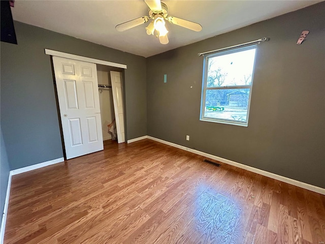 unfurnished bedroom with wood finished floors, a ceiling fan, visible vents, baseboards, and a closet