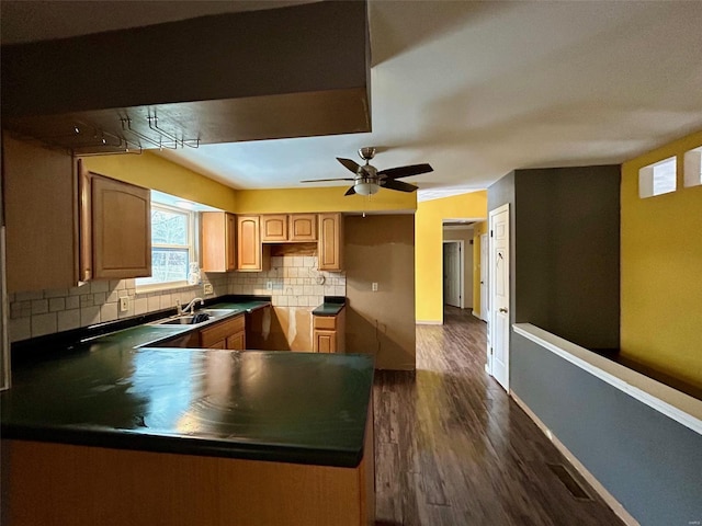 kitchen featuring baseboards, dark wood-style floors, a peninsula, a sink, and backsplash