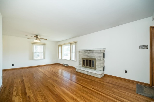 unfurnished living room with visible vents, a ceiling fan, wood finished floors, a stone fireplace, and baseboards