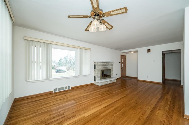 unfurnished living room with visible vents, a stone fireplace, ceiling fan, and wood finished floors