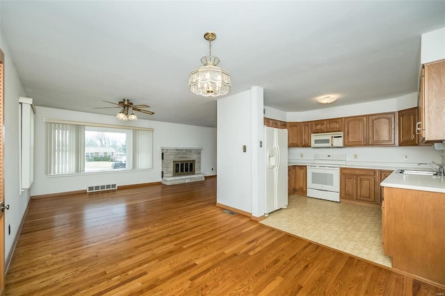 kitchen with visible vents, brown cabinets, a sink, open floor plan, and white appliances