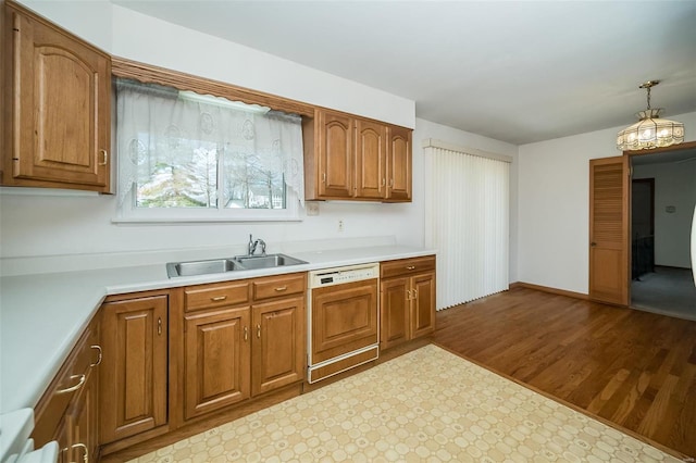 kitchen featuring brown cabinets, a sink, paneled dishwasher, light countertops, and hanging light fixtures