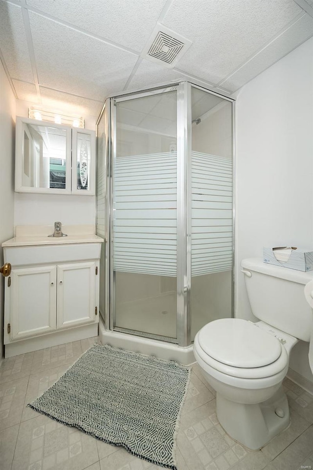 bathroom with visible vents, a drop ceiling, toilet, a stall shower, and vanity