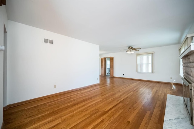 unfurnished living room featuring visible vents, baseboards, ceiling fan, a stone fireplace, and light wood-style floors